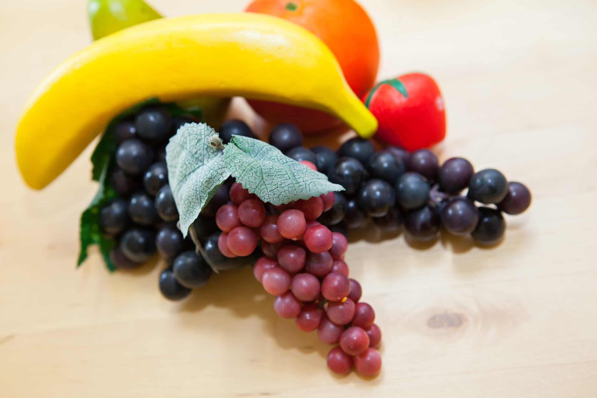 Obstmodelle aus der Ernährungsberatung: Banane, Trauben, Orange und Erdbeere auf einer Holzplatte.