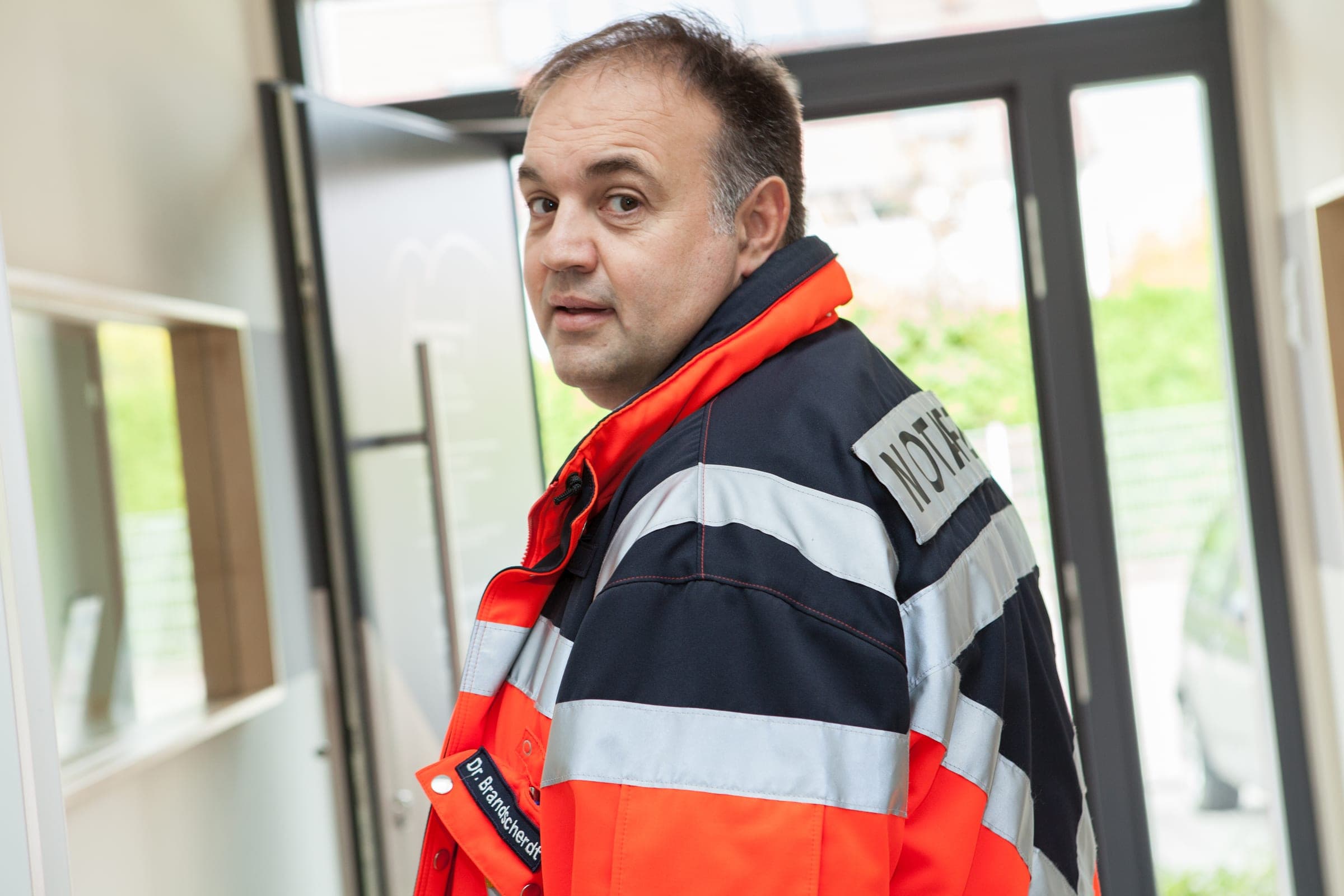 Dr. med. Bruno Brandscherdt in Notarztjacke im Eingangsbereich der Praxis.